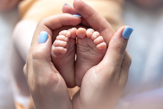 Mom holds the legs of a newborn baby in her hands.